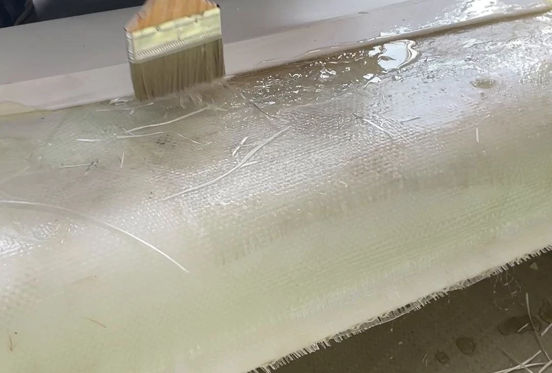 A brush applying resin to fibreglass cloth in a mould