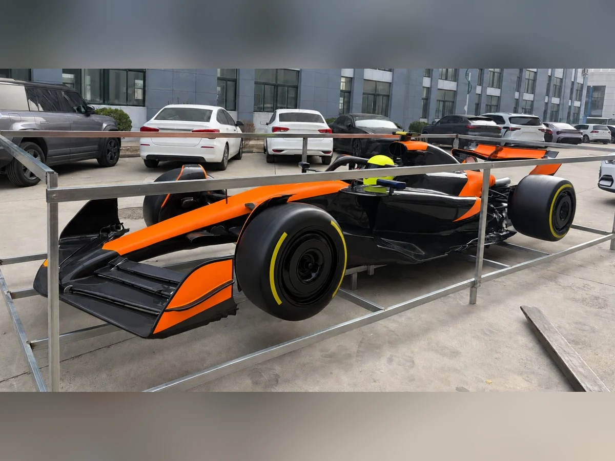 Formula-style show car in orange and black inside a transport frame, front three-quarter view, graphics removed
